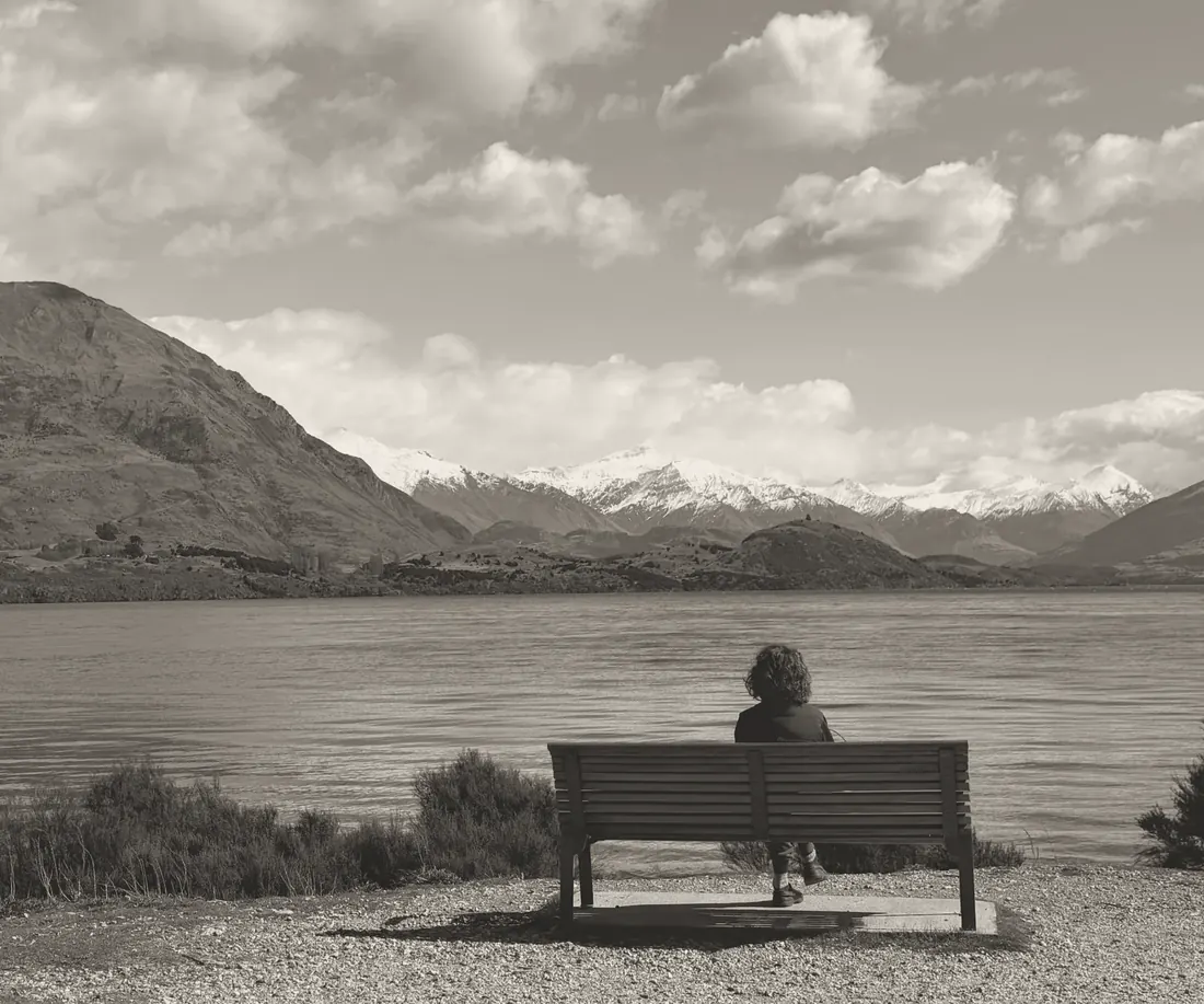 A person on a bench by Lake Wānaka, looking out at the mountains